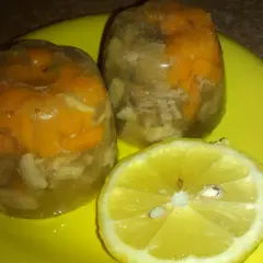 Galareta z kurzych łapek z marchewką i cytryną na żółtym talerzu.
